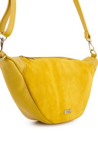 Żółta skórzana i zamszowa torba crossbody o zakrzywionym kształcie, z suwakiem i metalowym akcentem w postaci logo. Posiada odpinany pasek.