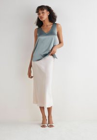 Šedý saténový top bez rukávů s výstřihem do V, spárovaný se světlou saténovou midi sukní. Hladká textura, minimalistický design a jemný lesk. Stříbrné sandály.