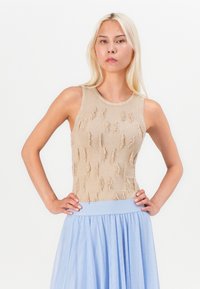 Beige strikket ermeløs topp med hevede frynser; kombinert med en lyseblå, luftig skjørt med elastisk midjebånd.