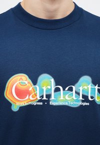 T-shirt in cotone blu navy con una grafica colorata e accenti in rosso, giallo e blu, inclusa la scritta "Carhartt" in bianco.