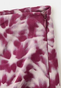 Približen posnetek tkanine s vijoličnim in belim vzorcem kravate in barve ter majhnim vijoličnim zadrgo na zgornjem robu.