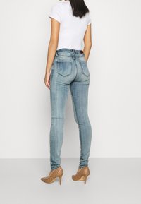 Mörka jeans i ljusblå denim, med hög midja, två bakfickor och en åtsittande silhuett, i kombination med bruna högklackade skor.