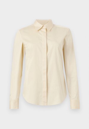 Kremfarvet langærmet skjorte med knapper, spids krave og skjult knapstolpe, vist på en ensfarvet baggrund.