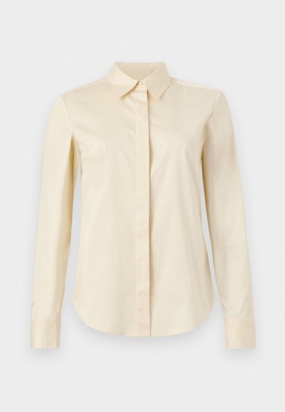 Μακρυμάνικο πουκάμισο εκρού με κλειστή σειρά κουμπιών και αιχμηρή γιακά, εμφανίζεται σε απλό φόντο.