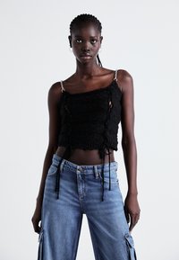 Čierny pletený crop top s nastaviteľnými šnúrkami a striebornými reťazovými ramienkami, kombinovaný so svetlomodrými širokými nohavicami obsahujúcimi vrecká a s gombíkovým zapínaním.