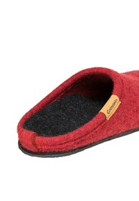 Red felt slipper with a black textured sole, open back, and a small brown label on the side. The fabric is soft and durable.