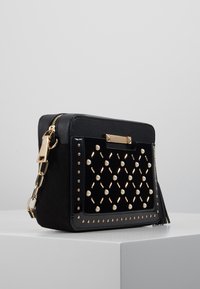 Czarna torebka podręczna o strukturalnym designie. Posiada mieszankę teksturowanych materiałów, złote okucia, perłowe akcenty oraz zamek błyskawiczny.
