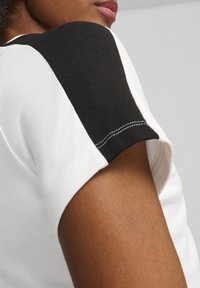 T-shirt met een witte stof en een zwarte schouderaccent; korte mouwen; zichtbare stiksels; gladde textuur.