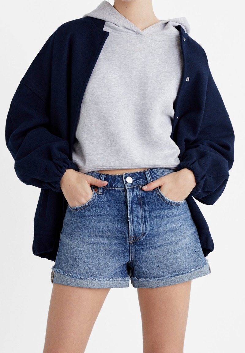 Laivastonsininen ylin takki harmaan hupparin päällä, yhdistettynä korkea vyötäröinen farkkushortsit. Sisältää käännettävät lahkeet ja sivutaskut.