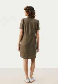 Kurzärmeliges, olivgrünes Leinenkleid mit geradem Schnitt, abgerundetem Saum und dezenten Schulterfalten, kombiniert mit weißen Sneakers.