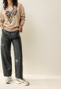 Sudadera beige con corazón de estampado de leopardo negro y texto dorado; combinada con pantalones anchos de cuero negro de tiro alto; zapatillas plateadas.