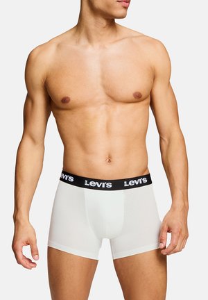 Männlicher Oberkörper, bekleidet mit weißen Levi's Boxershorts mit schwarzem Bund und weißem Levi's-Logo, vor neutralem Hintergrund posierend.