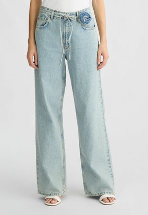 Jeans in denim azzurro chiaro a gamba larga con vita regolabile, dotati di un fiore decorativo in denim sulla tasca anteriore. Texture morbida e vestibilità comoda.
