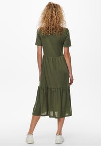 Olive green midi dress with short sleeves, tiered skirt, soft fabric, and a relaxed fit. Features a rounded neckline and subtle texture.