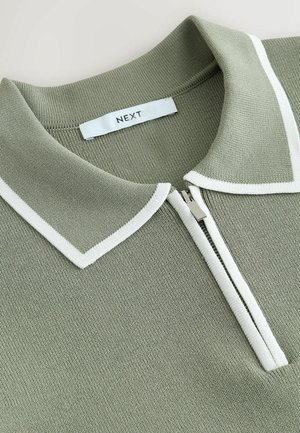 Vihreä teksturoitu poolopaita, jossa valkoinen kaulus ja vetoketjusomiste. Kauluksessa näkyy sisäpuolella "NEXT"-merkillä varustettu lappu.