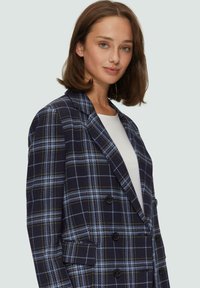 Dubbelzijdige blazer in marineblauwe ruit met blauwe en gele accenten, gemaakt van gestructureerde stof. Heeft lichte klepjes en voorzakken.