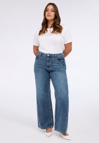 Lichtblauwe wijdlopende jeans met een hoge taille, voorzien van voorkneuzen en een gladde denimtextuur. Gepaard met een witte top met korte mouwen.