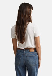 White cotton t-shirt with short sleeves, paired with medium blue denim jeans featuring a tan leather label on the waistband and back pockets.