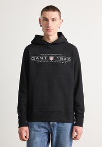 Felpa nera con cappuccio realizzata in un mix di cotone, con logo frontale bianco e rosso. Presenta un cappuccio con coulisse e polsini e orlo a coste.