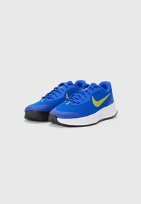 Sinised spordijalatsid, millel on võrkkangas pealis, kollane Swoosh logo, valge vaheplateau ja tekstureeritud must välispind. Sisaldab traditsioonilisi sidumispaelu.