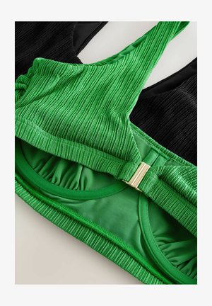 Czarno-zielony strój kąpielowy z textured ribbing i gładkim materiałem. Zawiera złoty zamek jako detal na zielonej części.