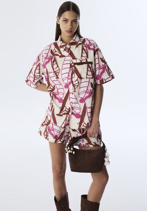 Camicetta a maniche corte con bottoni, caratterizzata da grafiche rosa e marroni su uno sfondo crema; abbinata a pantaloni corti coordinati e una borsa marrone con nappine.