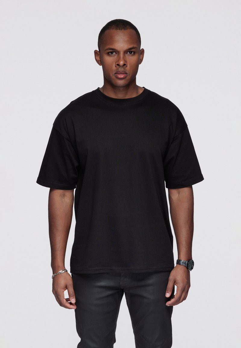 Musta lyhythihainen puuvillainen T-paita, jossa on klassinen pyöreä kaulus ja rento istuvuus. Yhdistetty tummiin farkkuihin ja rannekelloon.