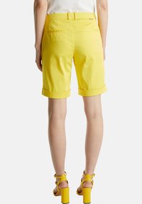 Pantalones cortos de algodón amarillos con dobladillos enrollados, que cuentan con bolsillos traseros y un cinturón a juego. Combinados con sandalias amarillas de tacón cuadrado.