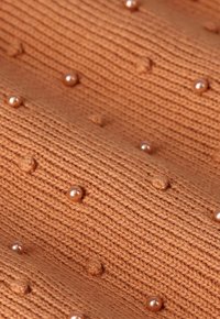 Tissu tricoté dans un brun chaud avec des points en relief et de petites perles roses brillantes intégrées tout au long, créant un motif texturé.