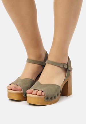 Sandalias de plataforma de ante verde con punta abierta, correa en el tobillo y tacón grueso. Presenta tachuelas metálicas decorativas y una textura superior suave.