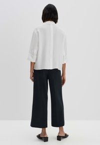 White textured shirt with a collar, loose fit, and cuffed sleeves paired with dark wide-leg pants and minimalist black sandals.