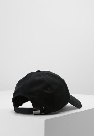 Schwarze Stoff-Basecap mit verstellbarem Riemen und Metallschnalle, liegend auf einer weißen Ecke vor einem einfarbigen hellgrauen Hintergrund.