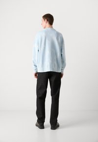 Sudadera azul claro con una textura suave y un sutil patrón nublado, combinada con pantalones gris oscuro y zapatos oscuros. Vista posterior.
