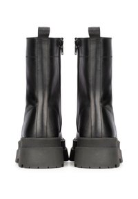 Bottes de cheville en cuir noir avec une finition lisse, des zips sur les côtés et des semelles épaisses en caoutchouc, comportant des détails de couture le long des coutures.