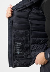 Sort dunjakke med quiltet design, vandafvisende og vindbeskyttende egenskaber. Interiørlabel med detaljer om materialer og plejeinstruktioner synlig.