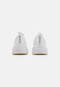 Adidași albi sport cu un material superior texturat, călcâi întărit și o talpă intermediară de culoare deschisă. Prezintă logo-ul "GUESS" pe partea din spate.