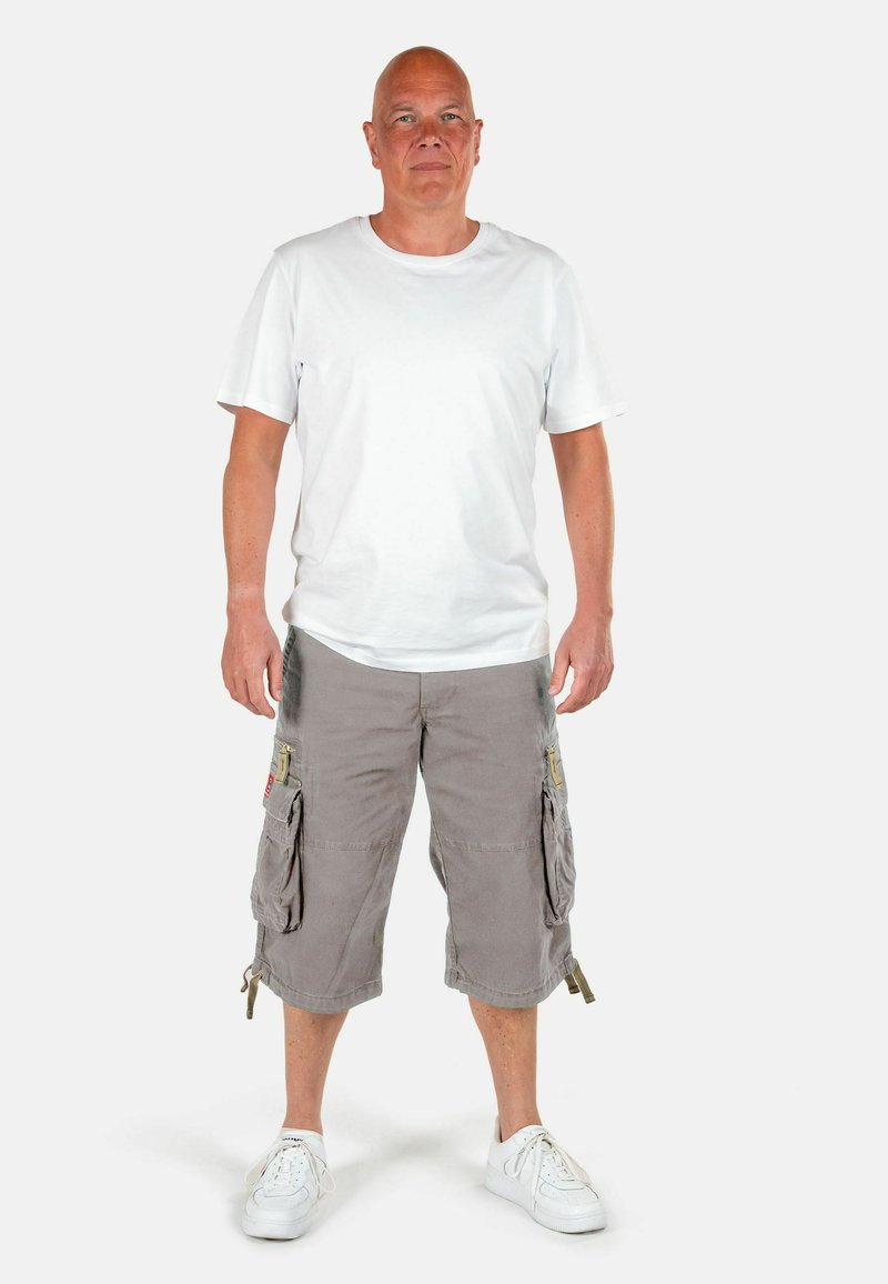 Pantaloni cargo grigi con profonde tasche laterali e orli con cordino, abbinati a una maglietta bianca a maniche corte e sneakers bianche.