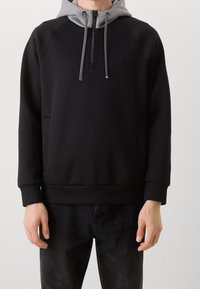 Sudadera negra con capucha gris, con cuello con cremallera, bolsillos frontales y mangas ajustadas. Textura suave con detalles de marca mínimos.