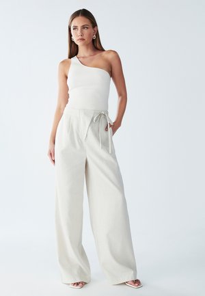 White ribbed one-shoulder top paired with light beige wide-leg trousers featuring a tie waist. Smooth fabric with subtle texture.
