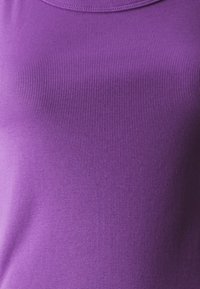 Zbliżenie na fioletowy top z prążkowanej tkaniny, ukazujący delikatną pionową teksturę i wysoki, zaokrąglony dekolt.