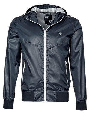 Veste légère à capuche bleu marine avec fermeture éclair blanche et poches zippées, poignets et ourlet côtelés, et logo discret sur la poitrine.