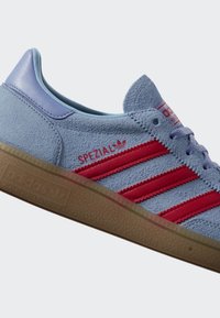 Světle modrá semišová teniska Adidas s červenými pruhy, gumovou podrážkou a nápisem "SPEZIAL" na boku.