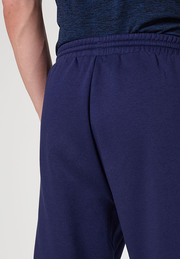 Close-up van een persoon die een marineblauwe joggingbroek en een donkerblauwe gemêleerde shirt draagt, waarbij de details van de elastische tailleband zichtbaar zijn.