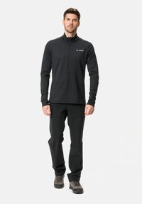 Pullover nero a maniche lunghe con colletto zip, abbinato a pantaloni neri e calzature grigie. Design semplice con logo del marchio sul petto.