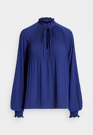 Blouse bleu roi à manches longues avec devant plissé, col haut à volants, fermeture à nouer et poignets volantés élastiqués sur fond uni.