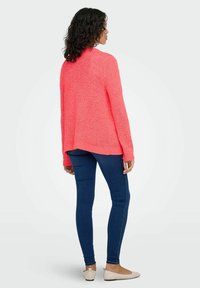 Pink knit sweater with a relaxed fit, textured yarn, ribbed cuffs, and hem, paired with blue skinny jeans and beige flats.