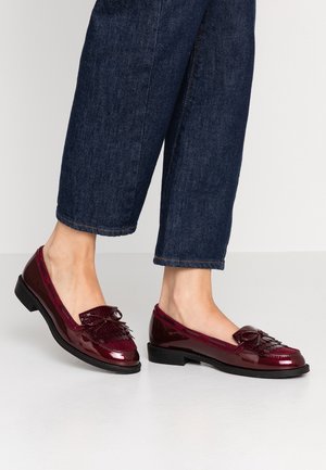 Bourgogne laklæder loafers med frynser og sløjfe, båret med cropped mørkeblå jeans på en lys grå gulv.