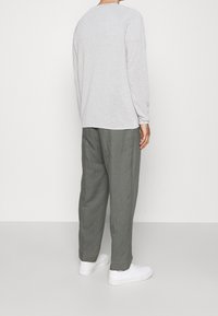 Chemise grise à manches longues associée à un pantalon vert ample et à des baskets blanches. Textures lisses, design décontracté et coupe relaxée.