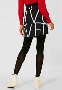 Svart kjol med djärv vit textdesign, tillverkad av mjukt material. Kombination med svarta strumpbyxor och vita texturerade ankelskor.