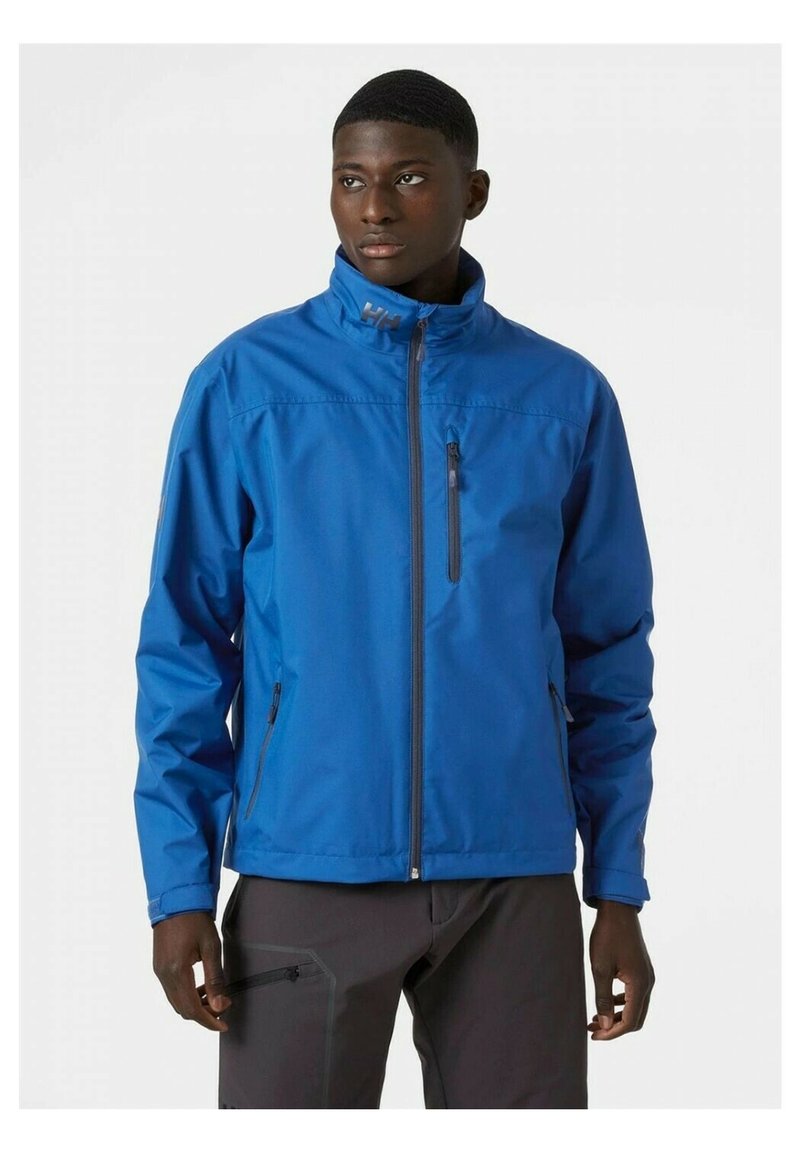 Blauwe waterdichte jas met een hoge kraag, volledige ritssluiting aan de voorkant en twee voorzakken. Beschikt over contrasterende grijze ritsen en logo-accenten.